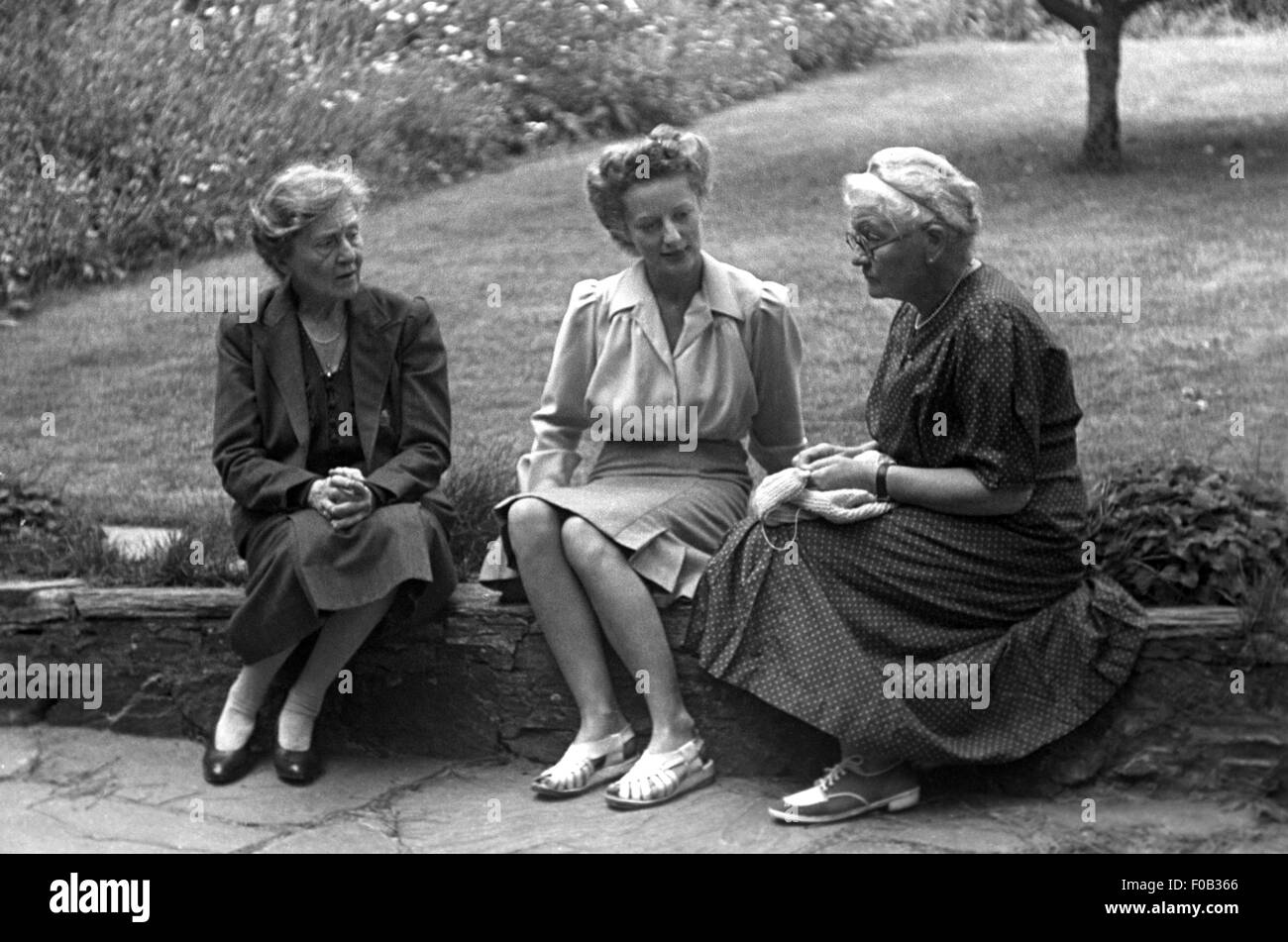 Two mature women and one middle aged woman sitting on a garden wall talking Stock Photo Alamy