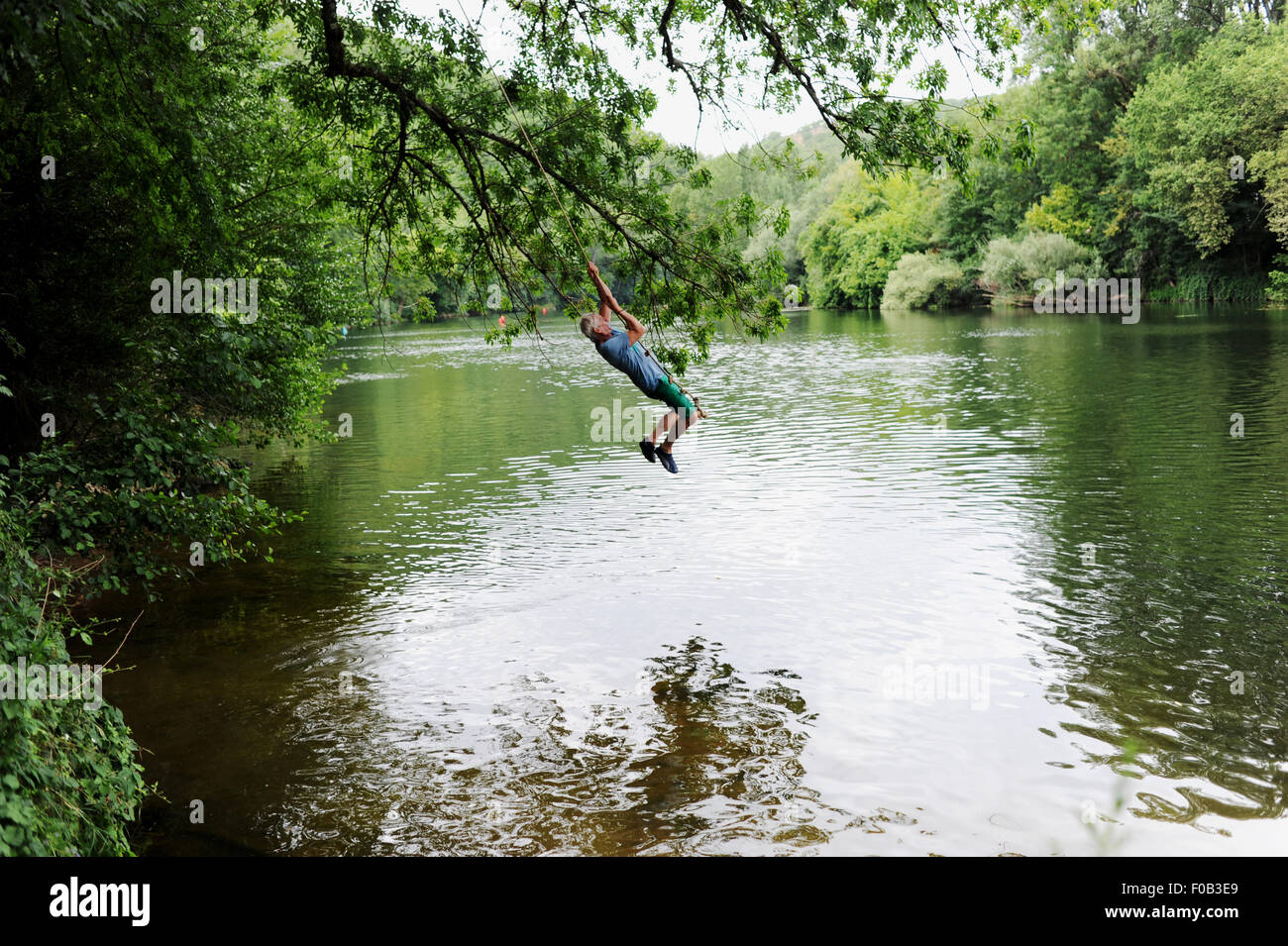 The River Lot in the Midi-Pyrenees area of France Europe Tourist male man swinging from a rope into the river Photograph taken by Simon Dack Stock Photo