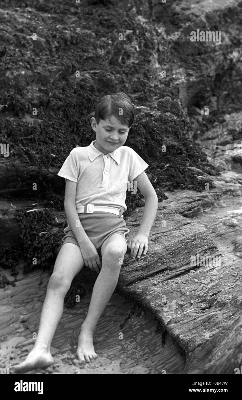 A young boy sitting on a rock at the seaside. Stock Photo