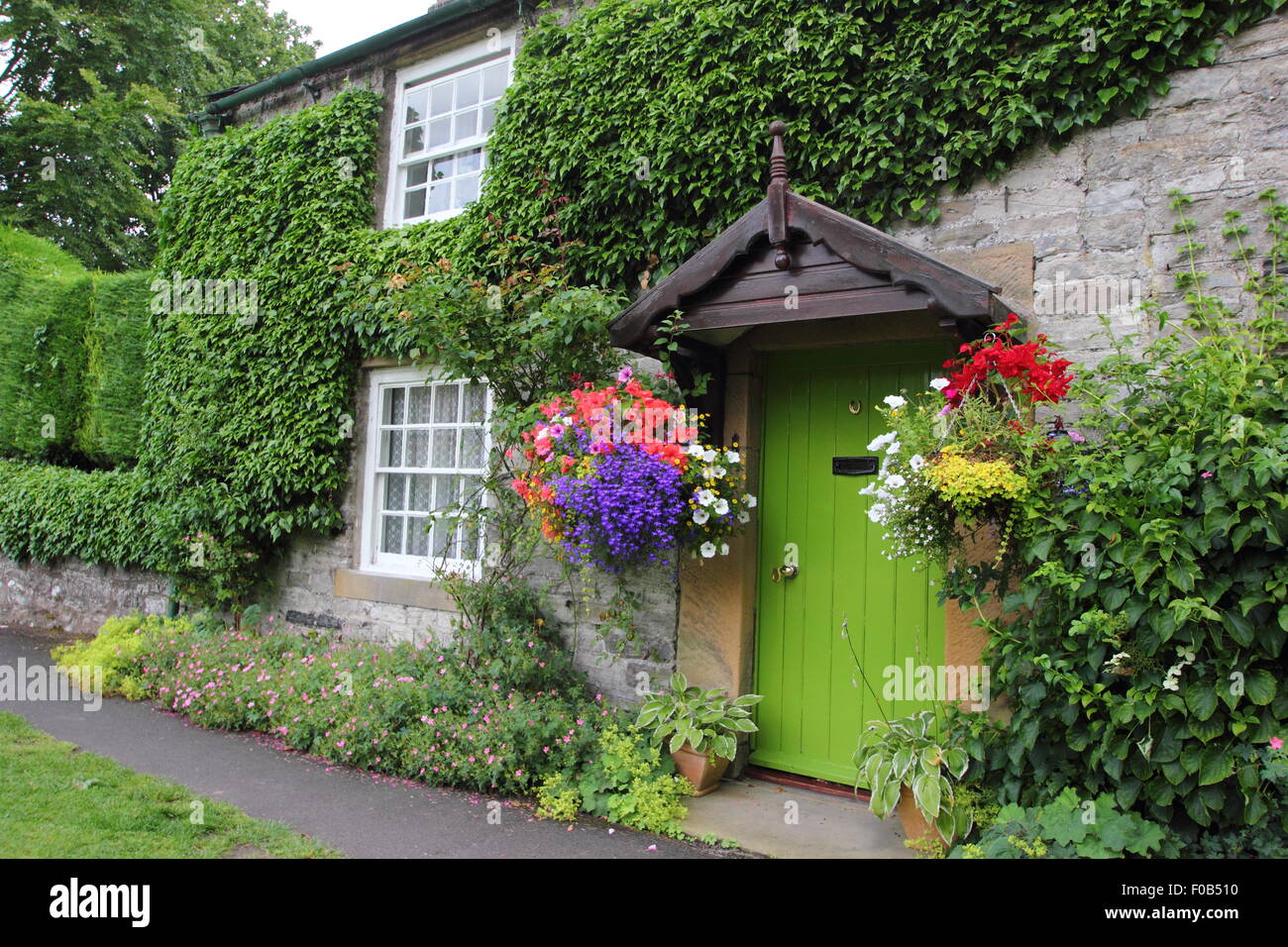 Hanging baskets frame the door to a traditional stone cottage in the Peak District, Derbyshire, England UK in summer Stock Photo