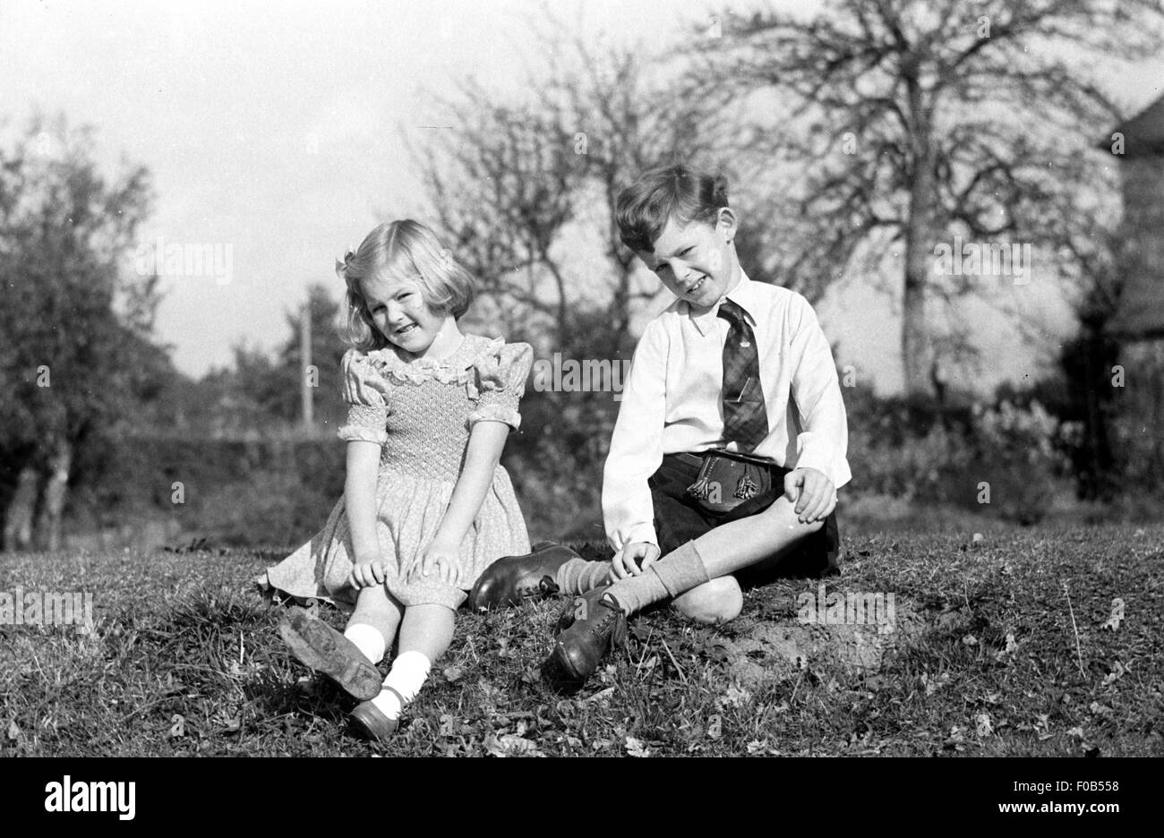 A little girl with blonde hair posing in the garden with her older brother Stock Photo