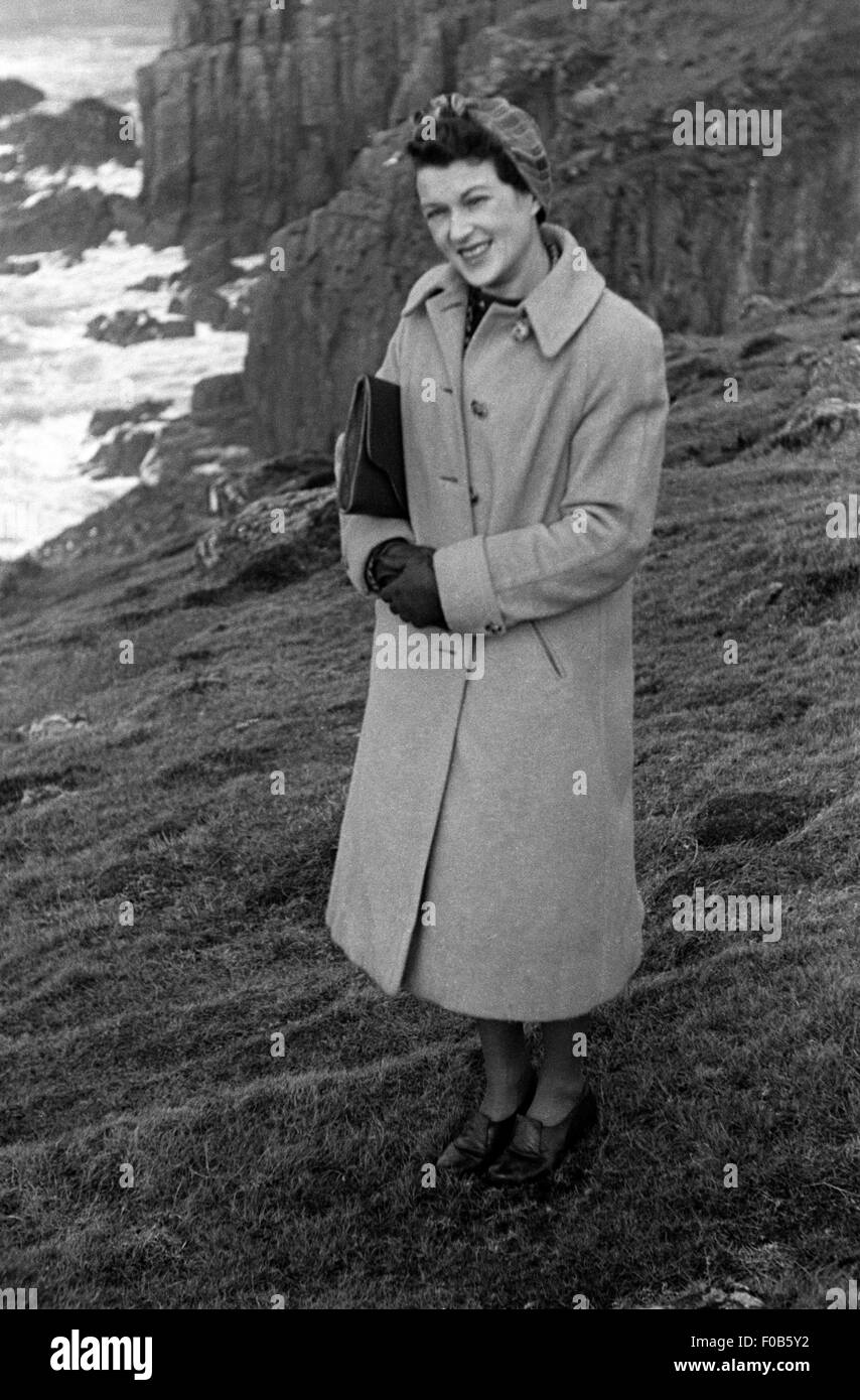 A woman wearing a coat and a headscarf stands at the edge of a high cliff Stock Photo
