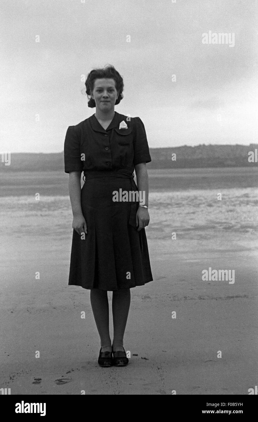 A young woman in a dark dress standing on a deserted beach Stock Photo