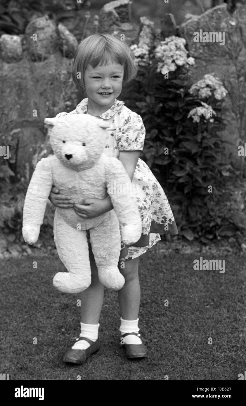 A fair haired little girl in a dress with a large teddy bear in a garden Stock Photo