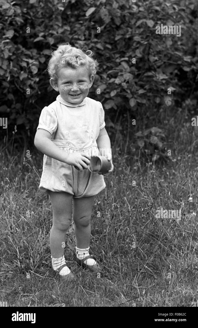 A Little Boy With Curly Hair Holding A Cup Standing In A Garden