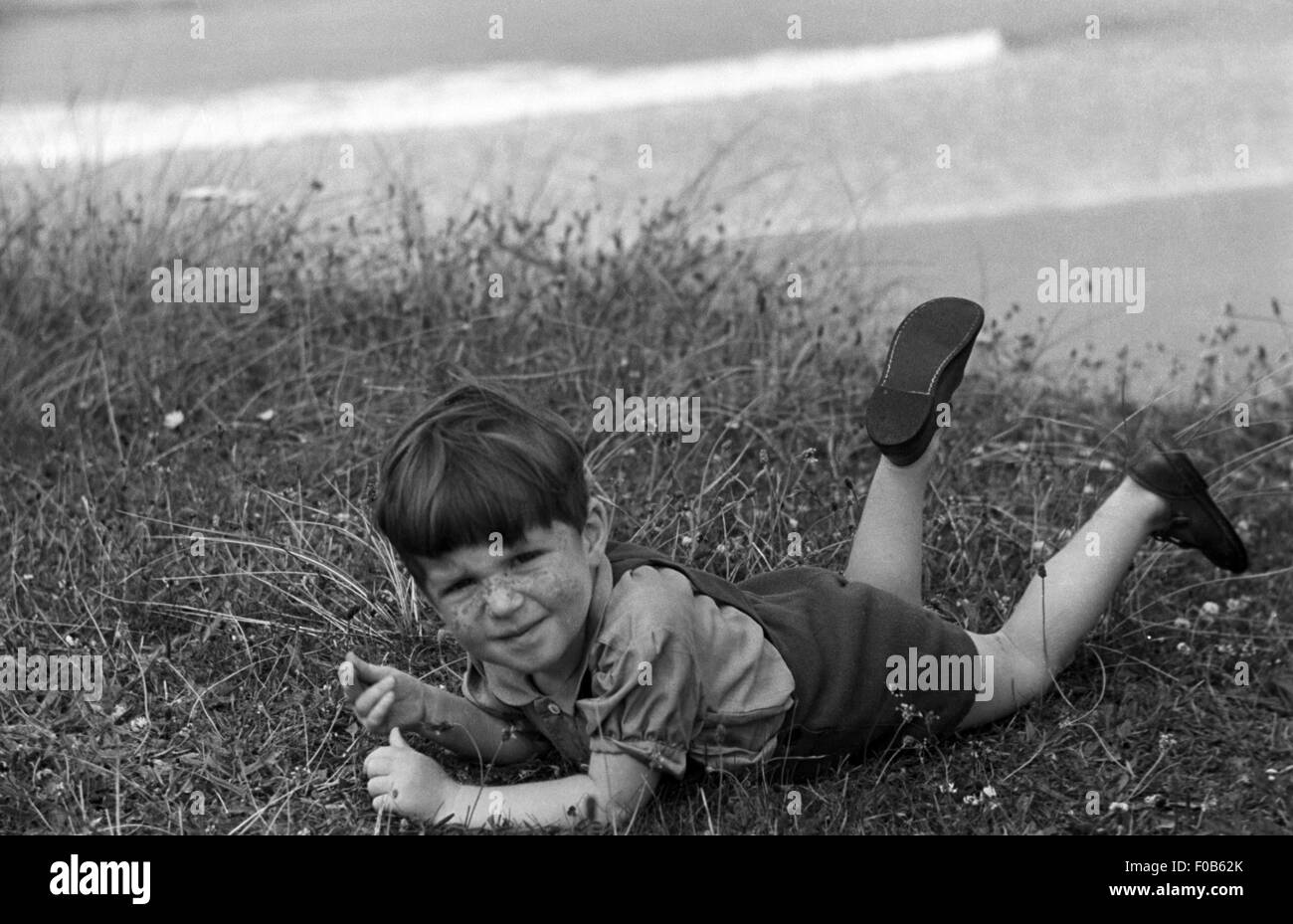 Dark haired little boy lying on grass at the seaside Stock Photo