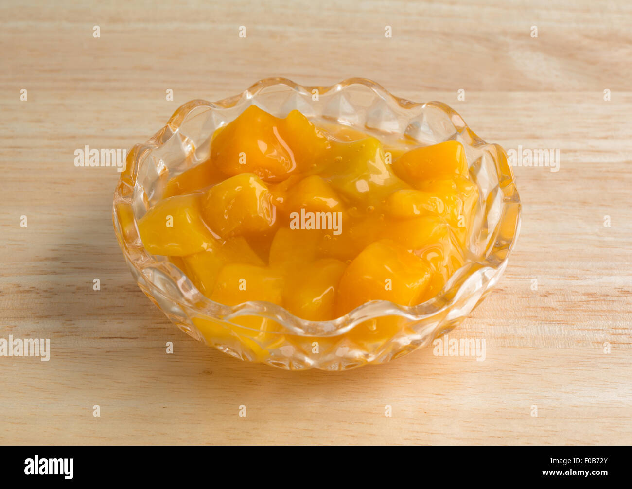A small bowl of diced peaches in heavy syrup on a wood table top illuminated with natural light. Stock Photo