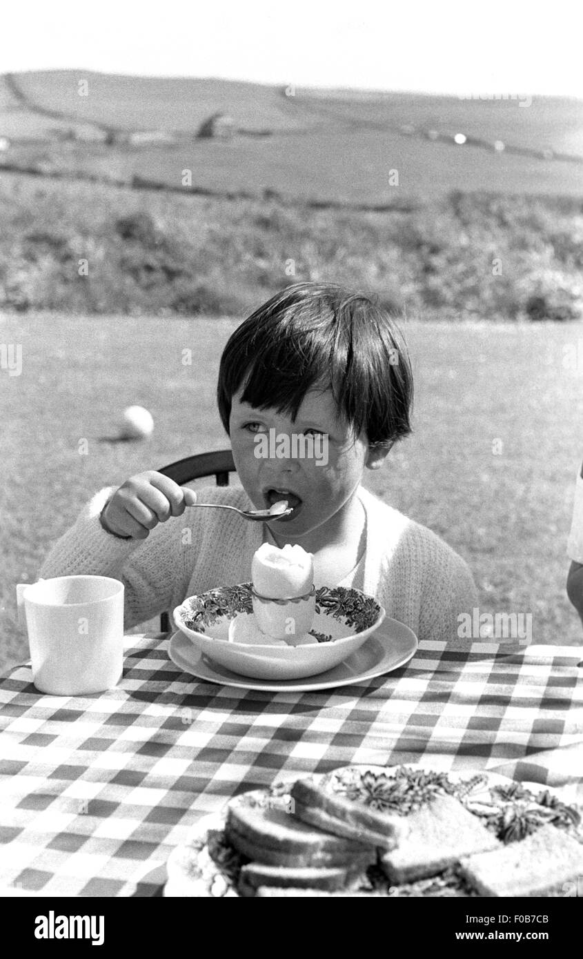 A young girl sitting at the table eating a boiled egg in the garden Stock Photo