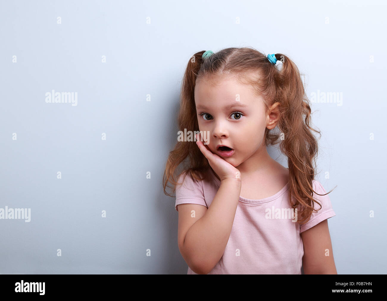 Cute funny kid girl surprising with open mouth on blue background Stock Photo