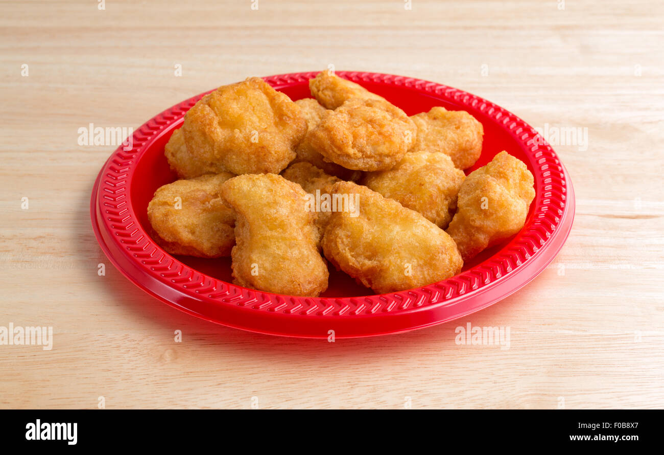 A serving of chicken nuggets on a red plate on a wood table top