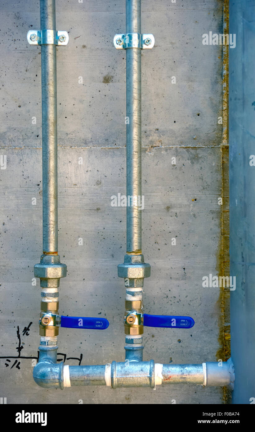 Galvanized steel tubes mounted on a concrete wall with its stopcocks Stock Photo