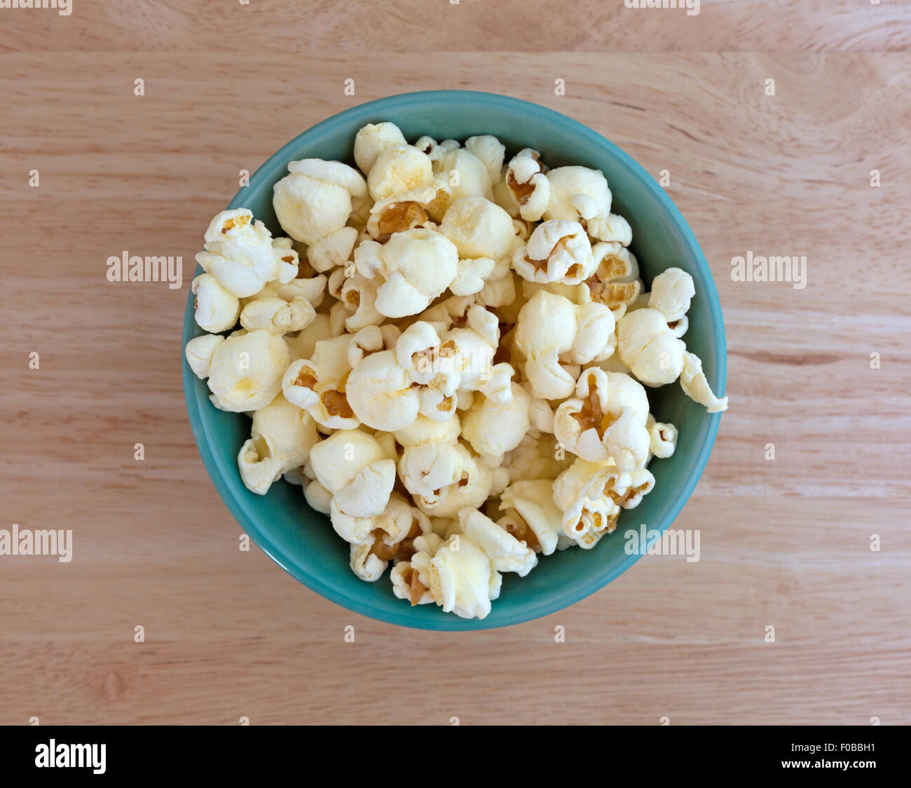Top view of a small bowl filled with a serving of white cheddar cheese flavored popcorn on a wood table top Stock Photo