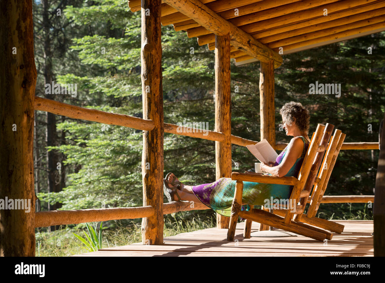 Woman reading a book on the porch of a log cabin at the Minam River Lodge in Oregon's Wallowa Mountains. Stock Photo