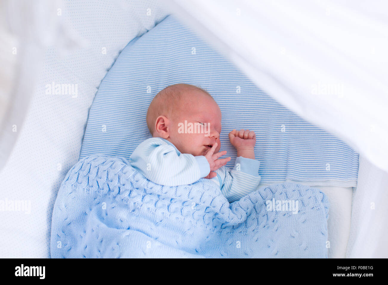 Newborn baby boy in bed. New born child sleeping under a blue knitted