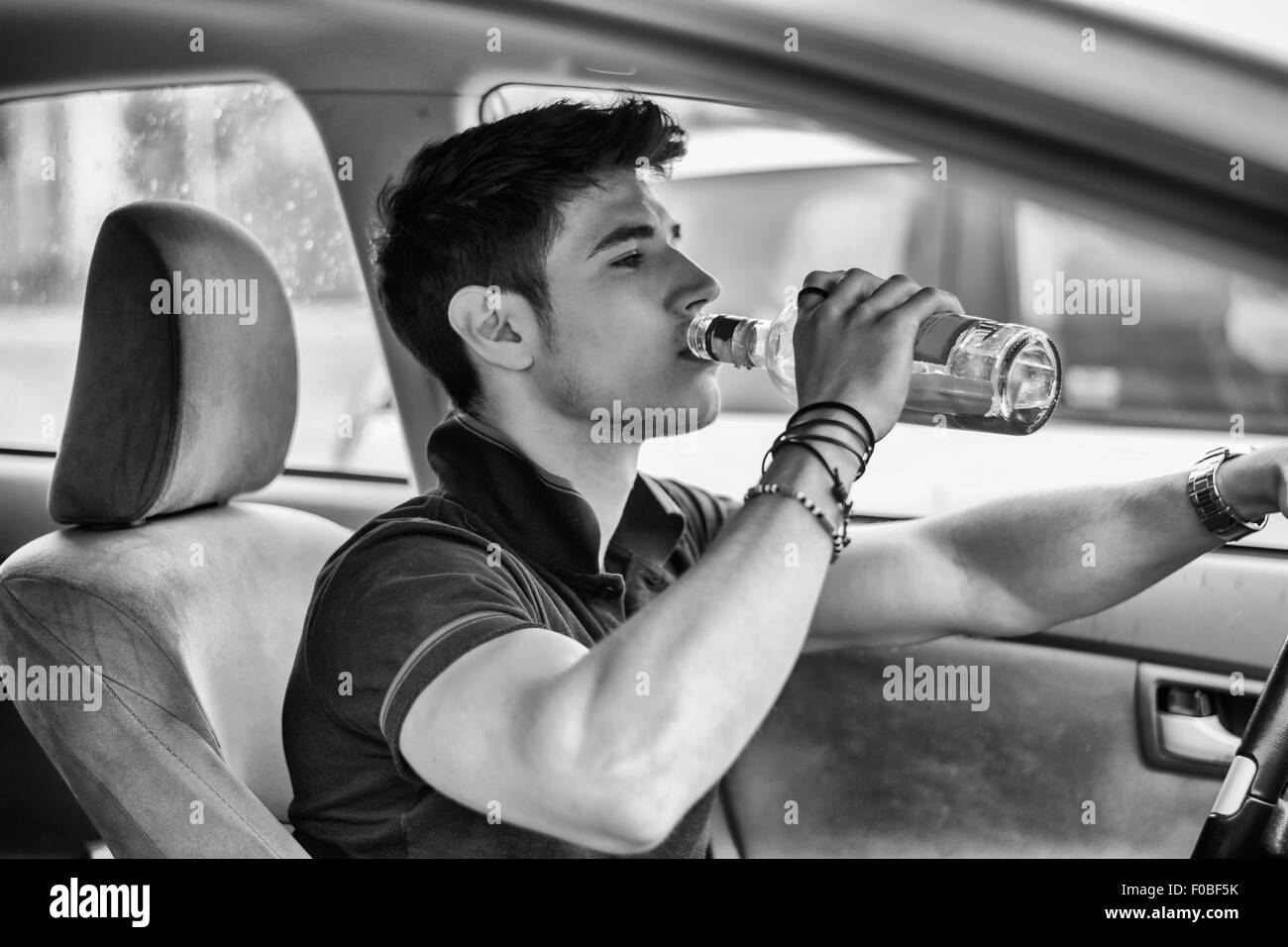 Young handsome man driving his car while drinking alcohol in the traffic. Black and white photo Stock Photo