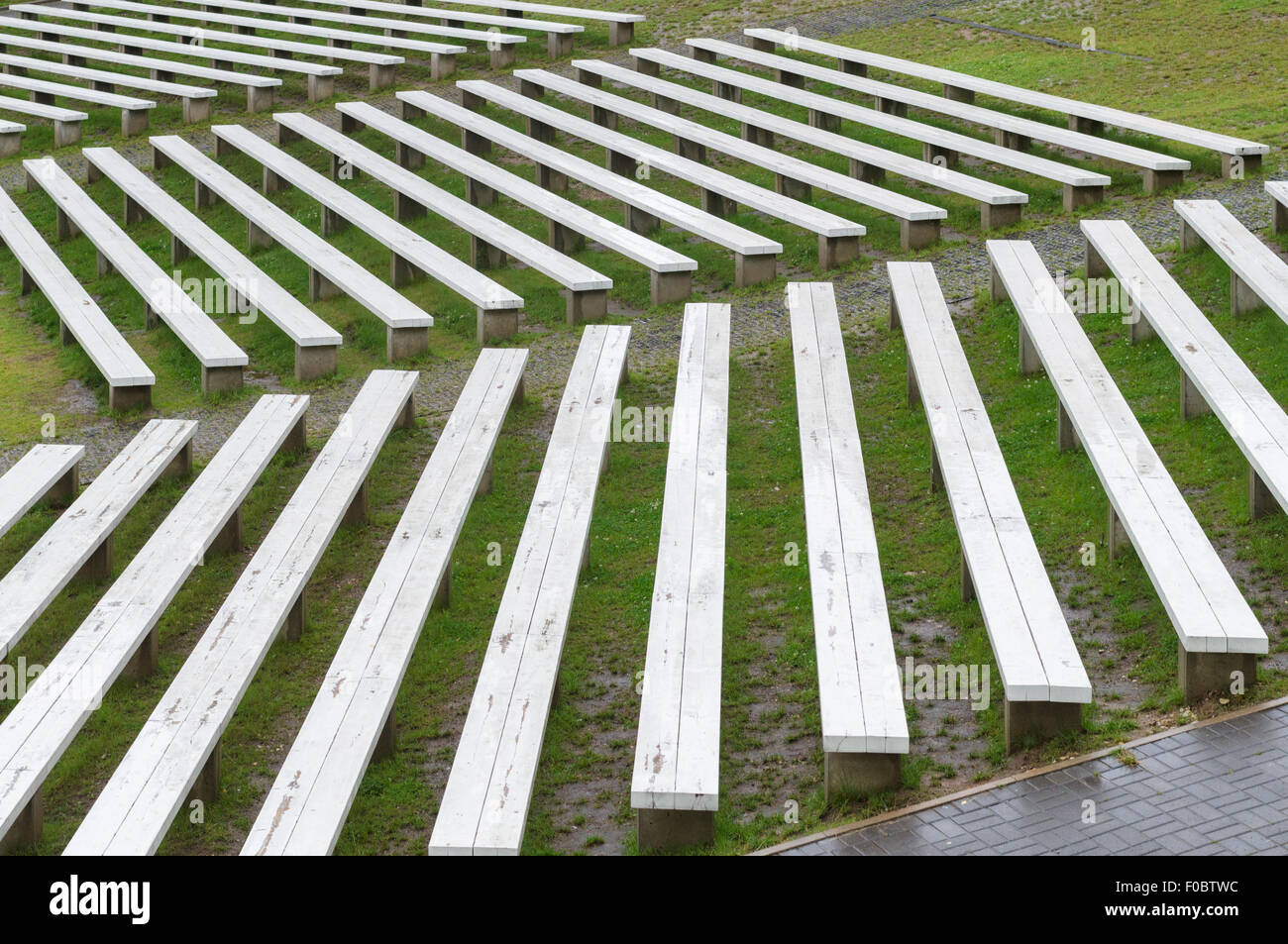 Rows of wooden benches on hillside of outdoor concert area, wet seats