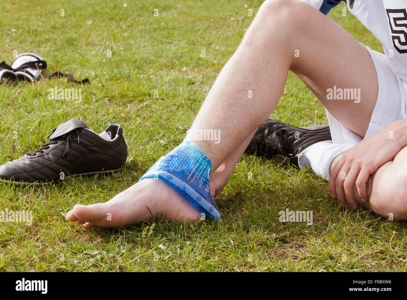 Low section of soccer player applying ice pack on ankle in field Stock Photo
