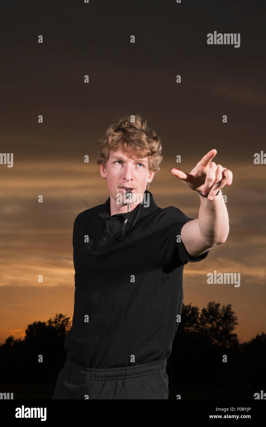 Referee blowing whistle while pointing away during sunset Stock Photo