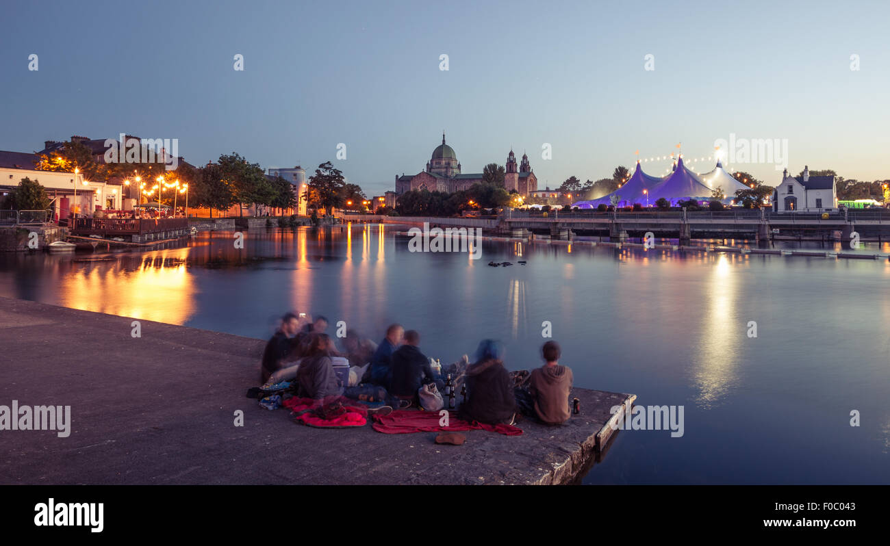 Group of people enjoy the evening during Galway Art Festival with 'Big Top' and Cathedral on the bank of Corrib river in Galway, Stock Photo
