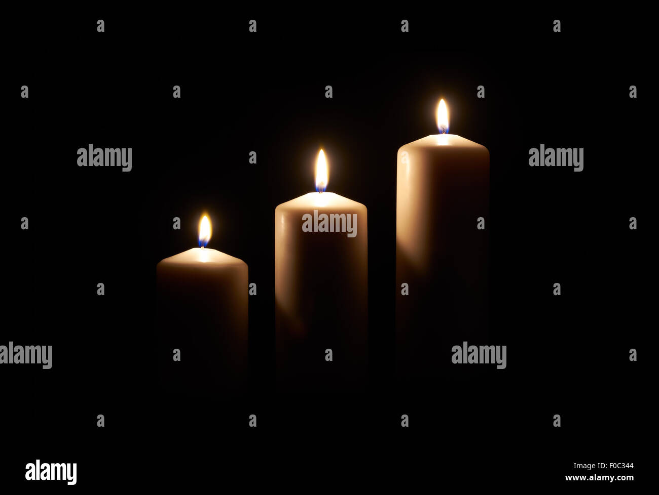 Lit white candles on a dark wooden floor with black background. Stock Photo