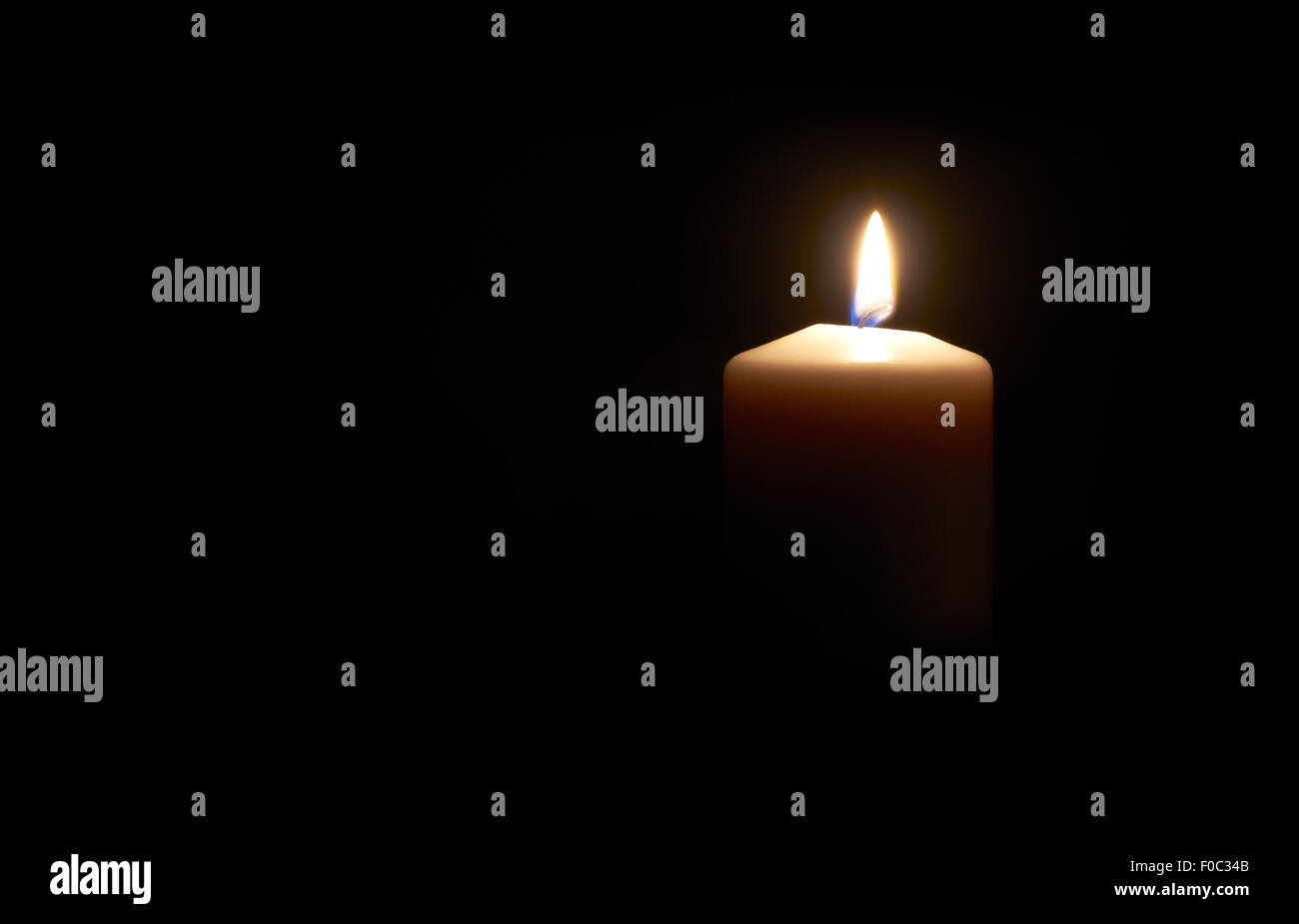Lit white candle on a dark  black background. Stock Photo