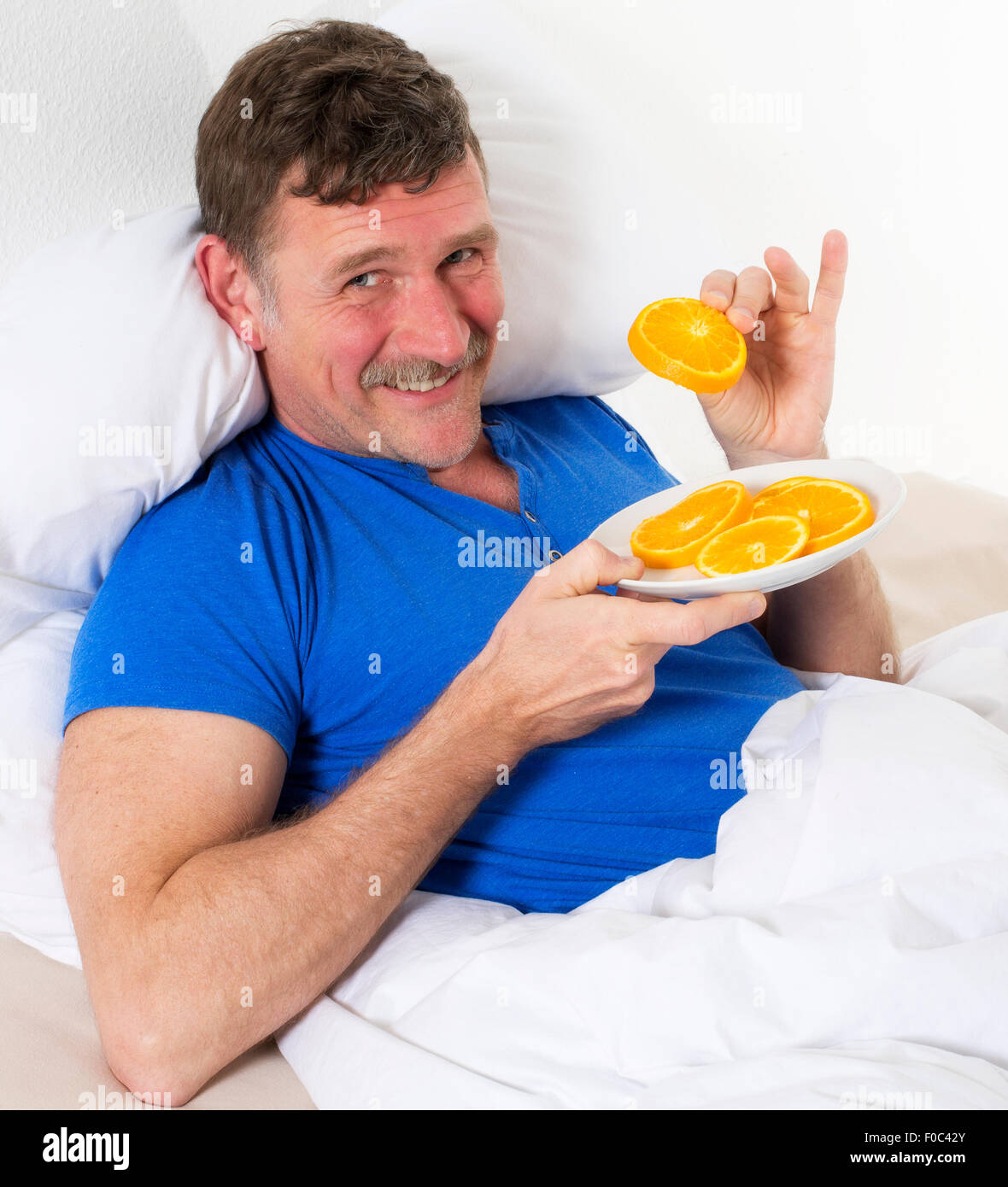 man in bed eating slice of oranges Stock Photo Alamy