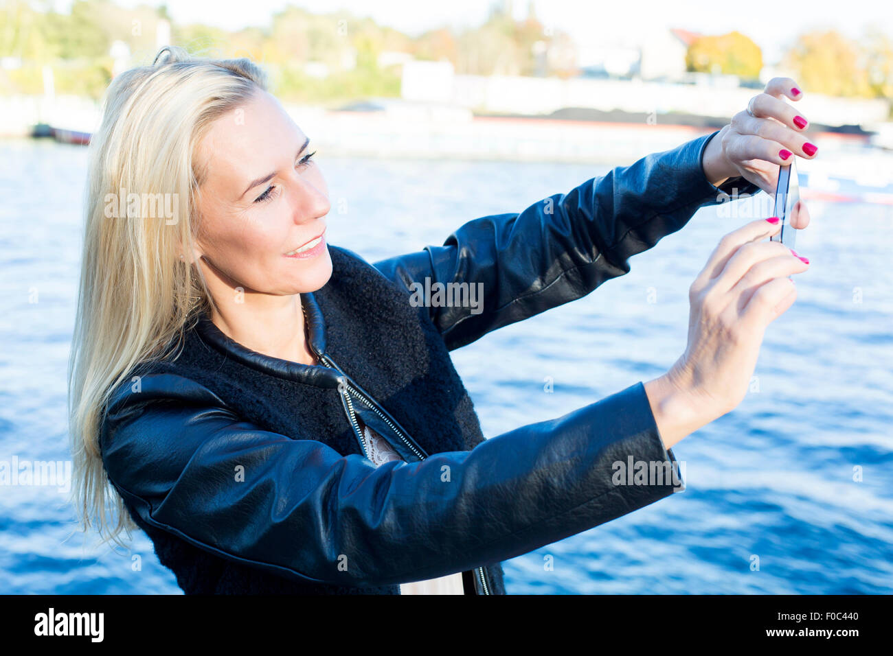 blond woman by the waterfront taking a selfie Stock Photo - Alamy
