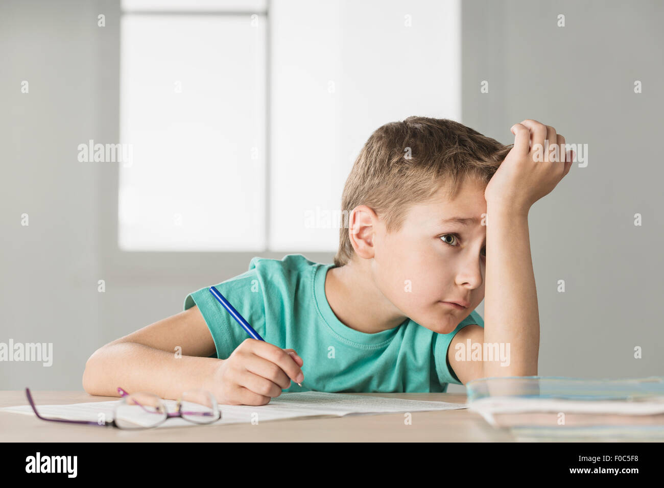 Bored boy with hand on forehead doing homework at home Stock Photo