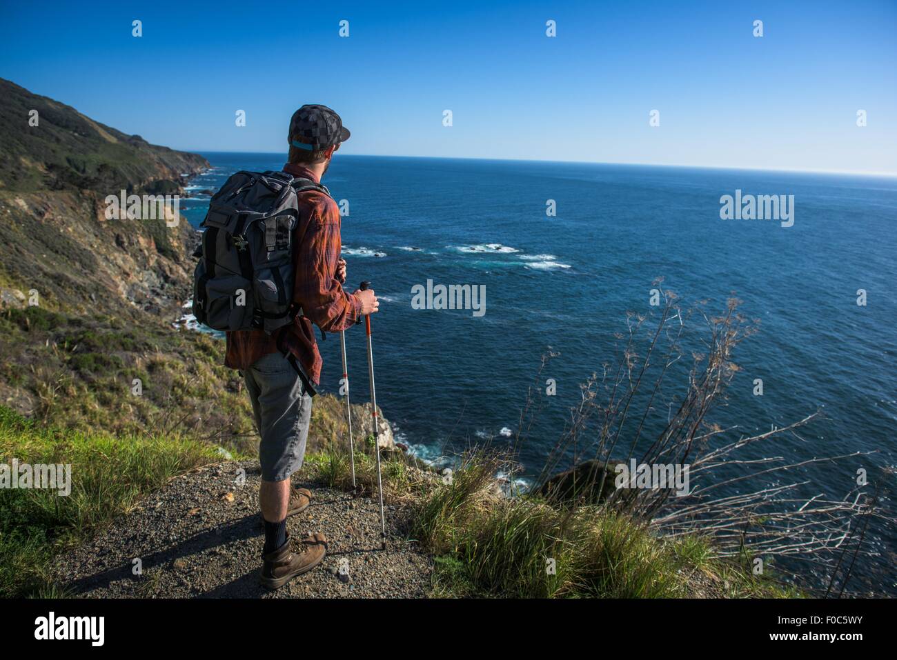 Young male hiker looking out from cliff top, Big Sur, California, USA Stock Photo