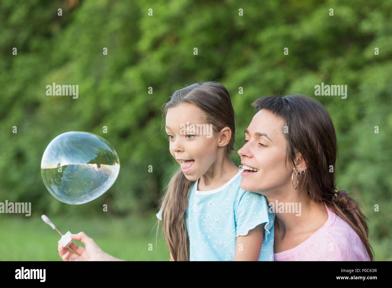 Mother and daughter playing with soap bubble outdoors Stock Photo