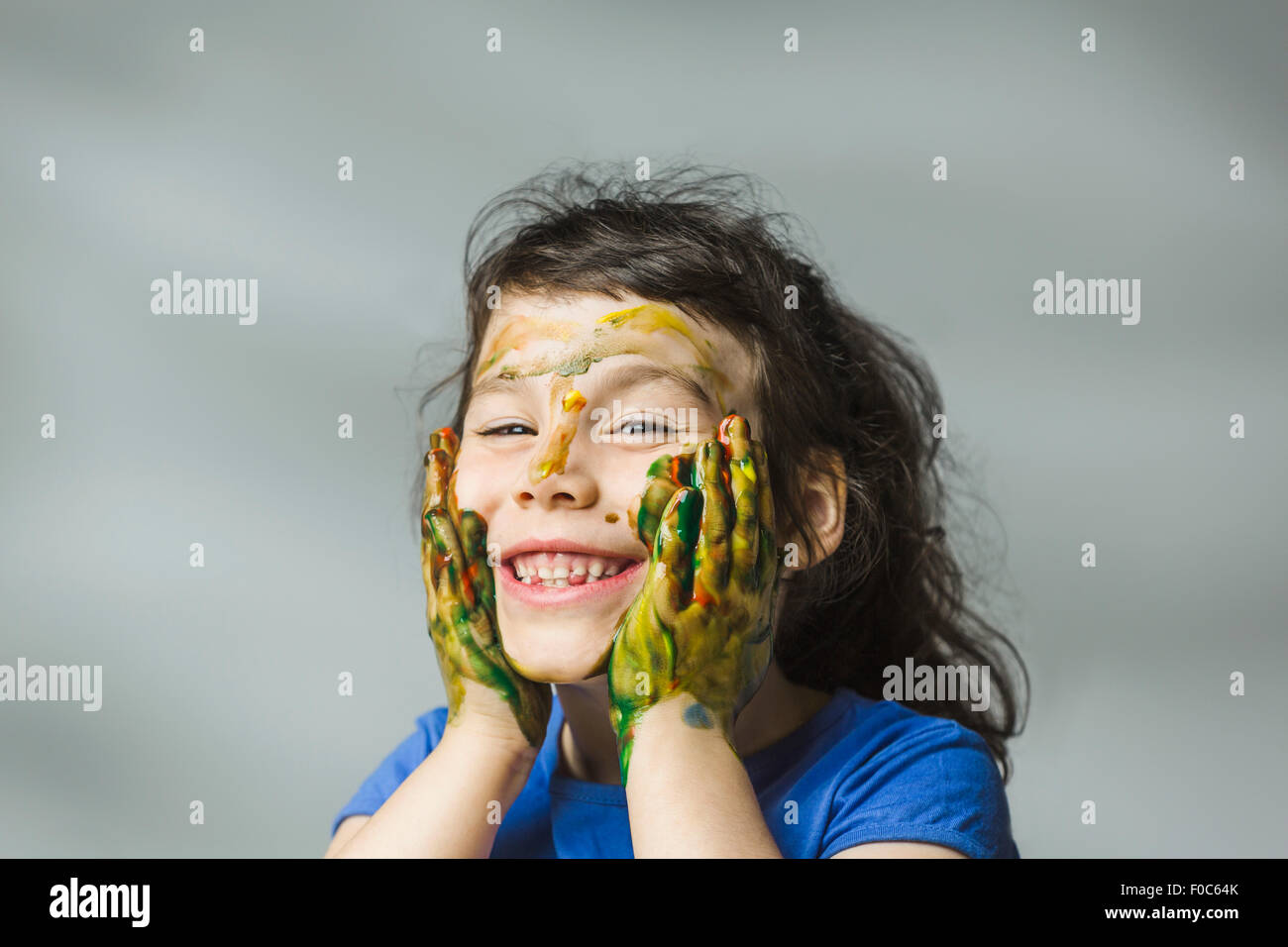 Smiling girl with painted face and hands over gray background Stock Photo