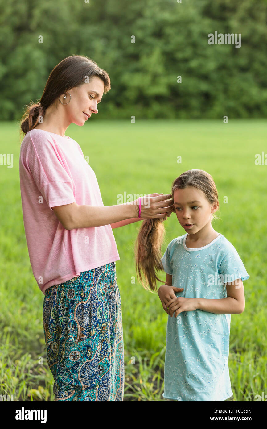 Mother making daughter's hair on field Stock Photo