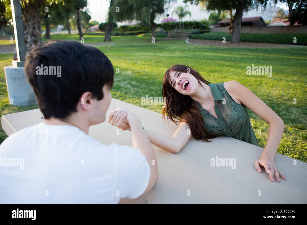 Young couple pretending to arm wrestle at picnic bench in park Stock Photo