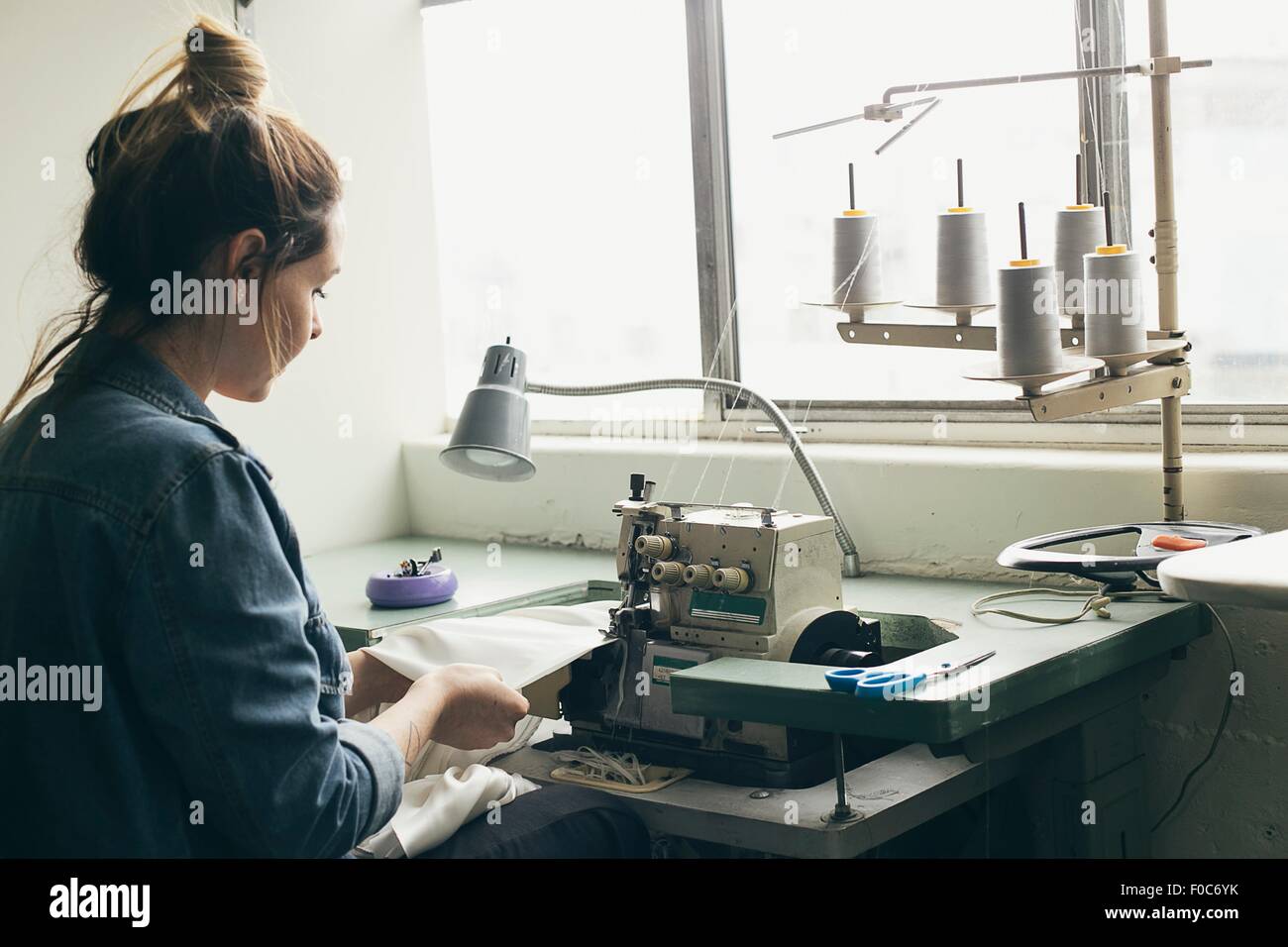 Young female seamstress sewing textile on sewing machine Stock Photo