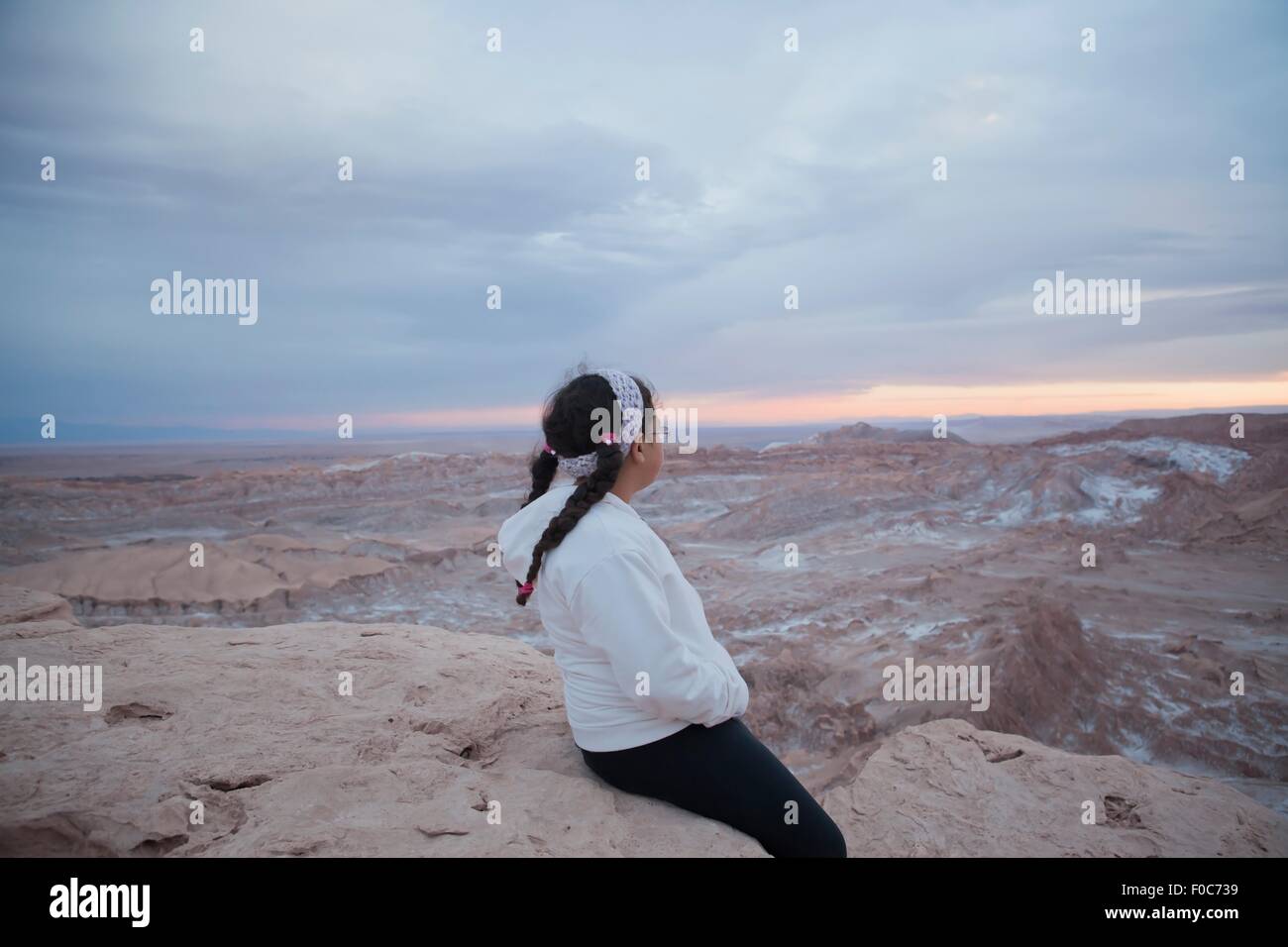 Young girl sitting on rock looking at view, Valley of the Moon, San Pedro. Atacama. Chile Stock Photo