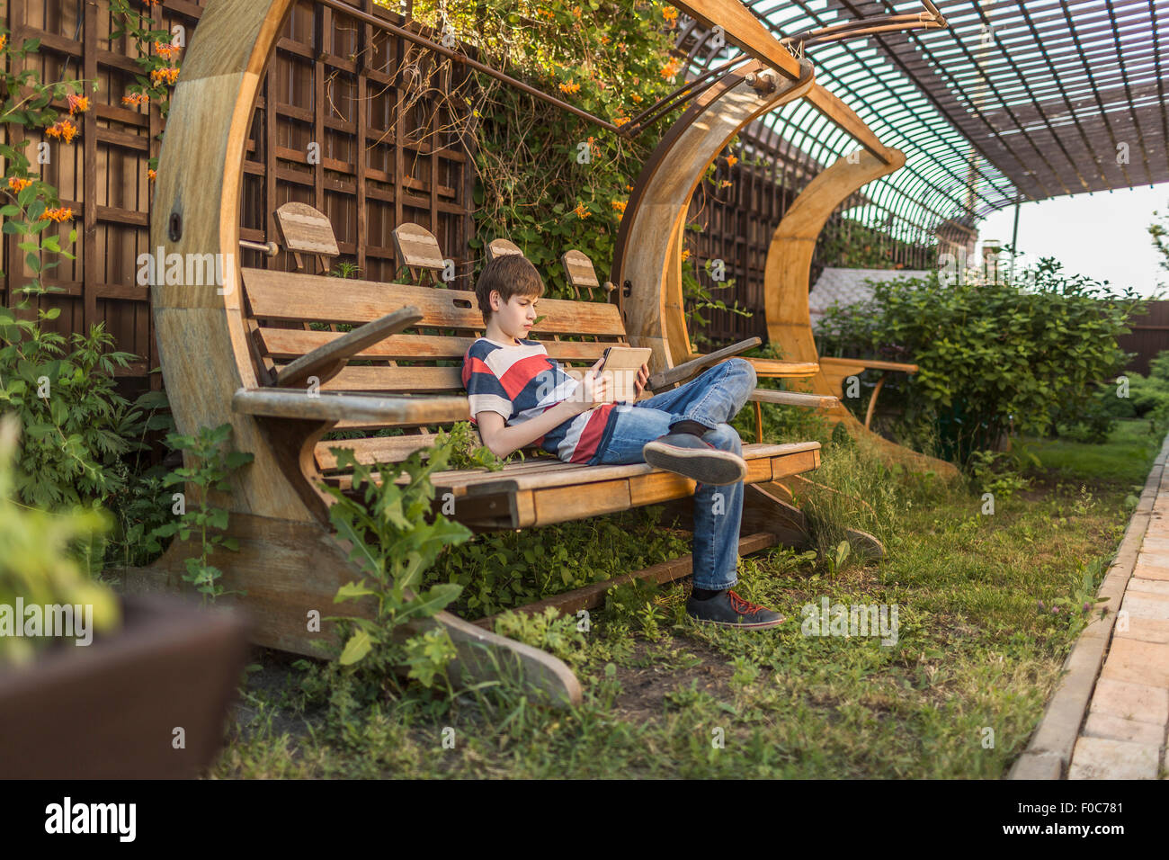 Full length of boy using digital tablet while sitting on bench in backyard Stock Photo