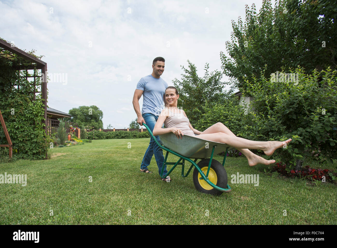 Man pushing girlfriend in wheelbarrow at backyard Stock Photo