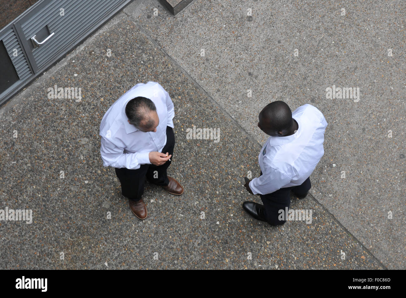 two men in white shirts from above talking and smoking Stock Photo