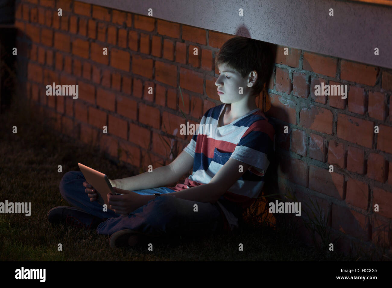 Boy using digital tablet while leaning against brick wall Stock Photo