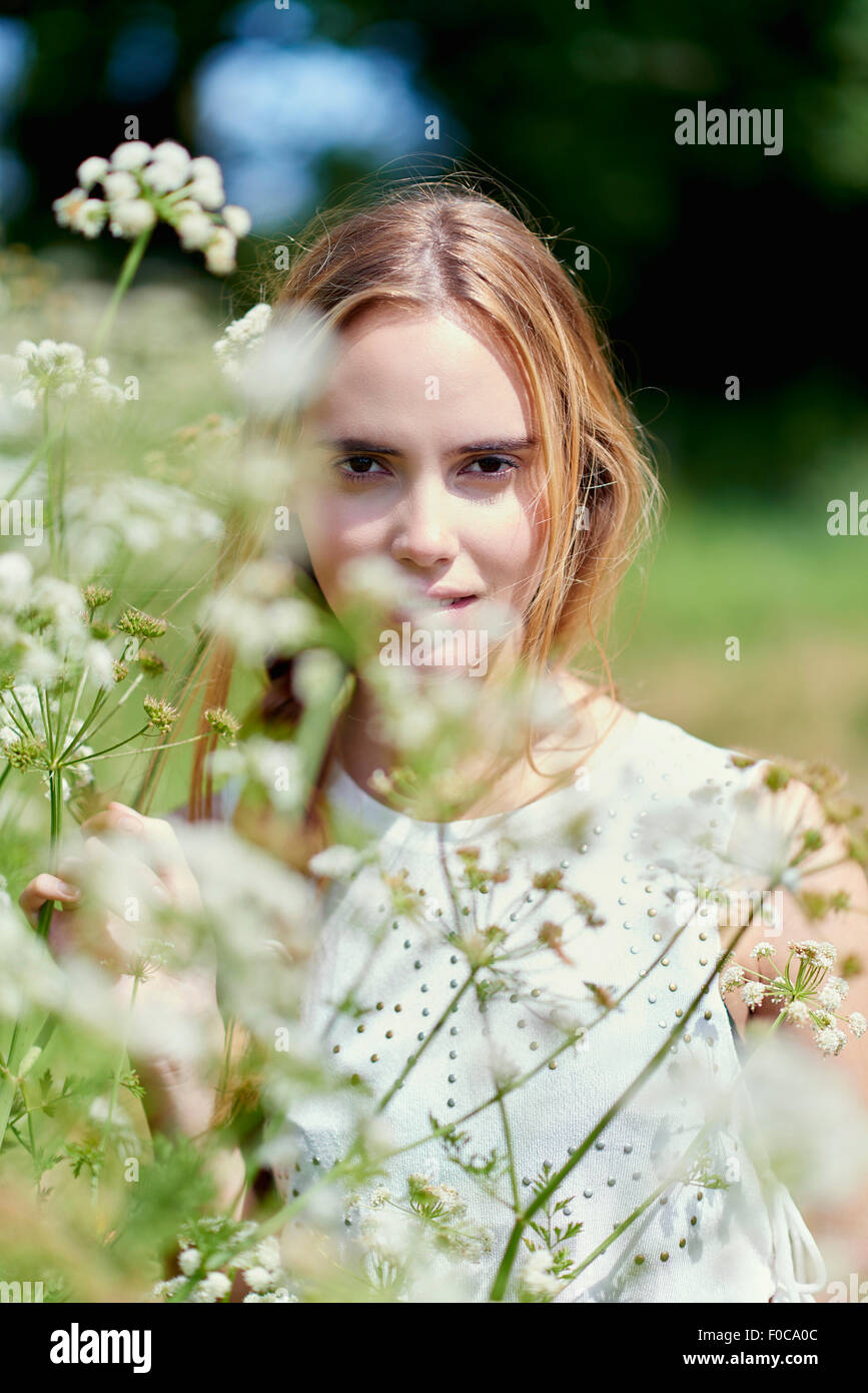 Portrait of young woman standing by flower plants in park Stock Photo ...