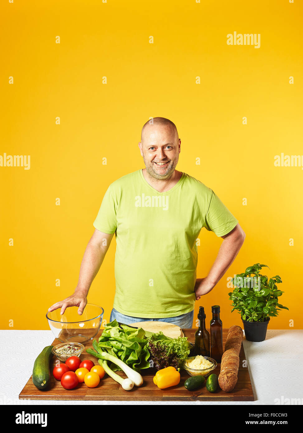 Fresh salad ingredients on the table, middle-aged man -  copy space and yellow background Stock Photo