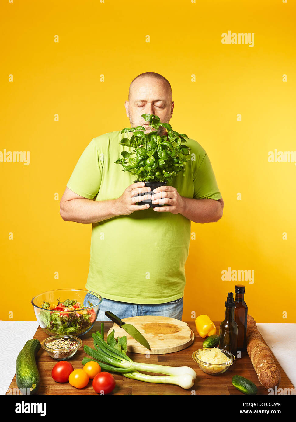 Fresh salad ingredients on the table, middle-aged man sniffs basil leaves  -  copy space and yellow background Stock Photo