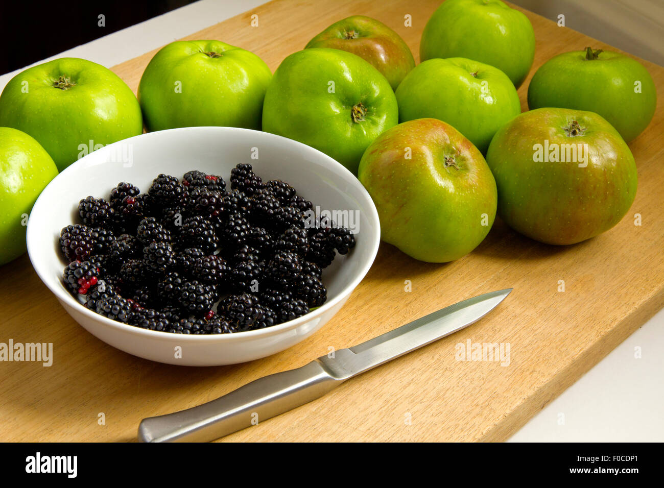 Bramley's Apples with Blackberries in white bowl with knife on wooden chopping board Stock Photo