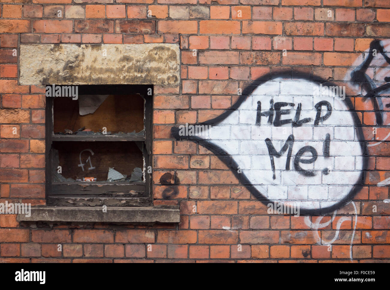 'Help Me!' graffiti words written in speech bubble painted next to coming from boarded up window derelict building red brick wal Stock Photo