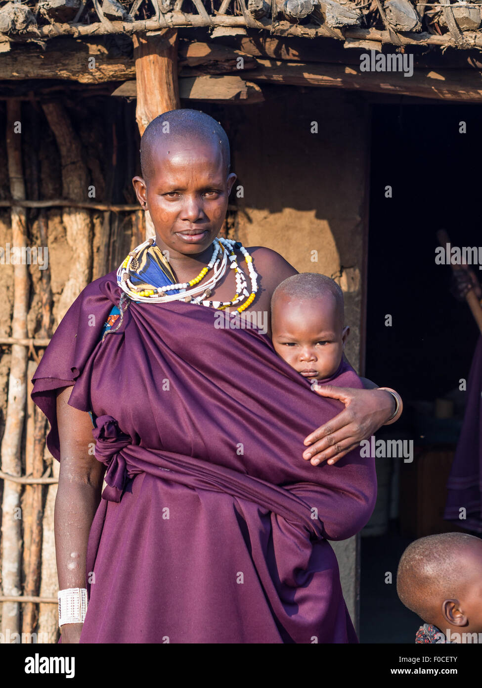 Maasai mother with her child in front of a traditional house in their boma (village) in Tan Stock Photo