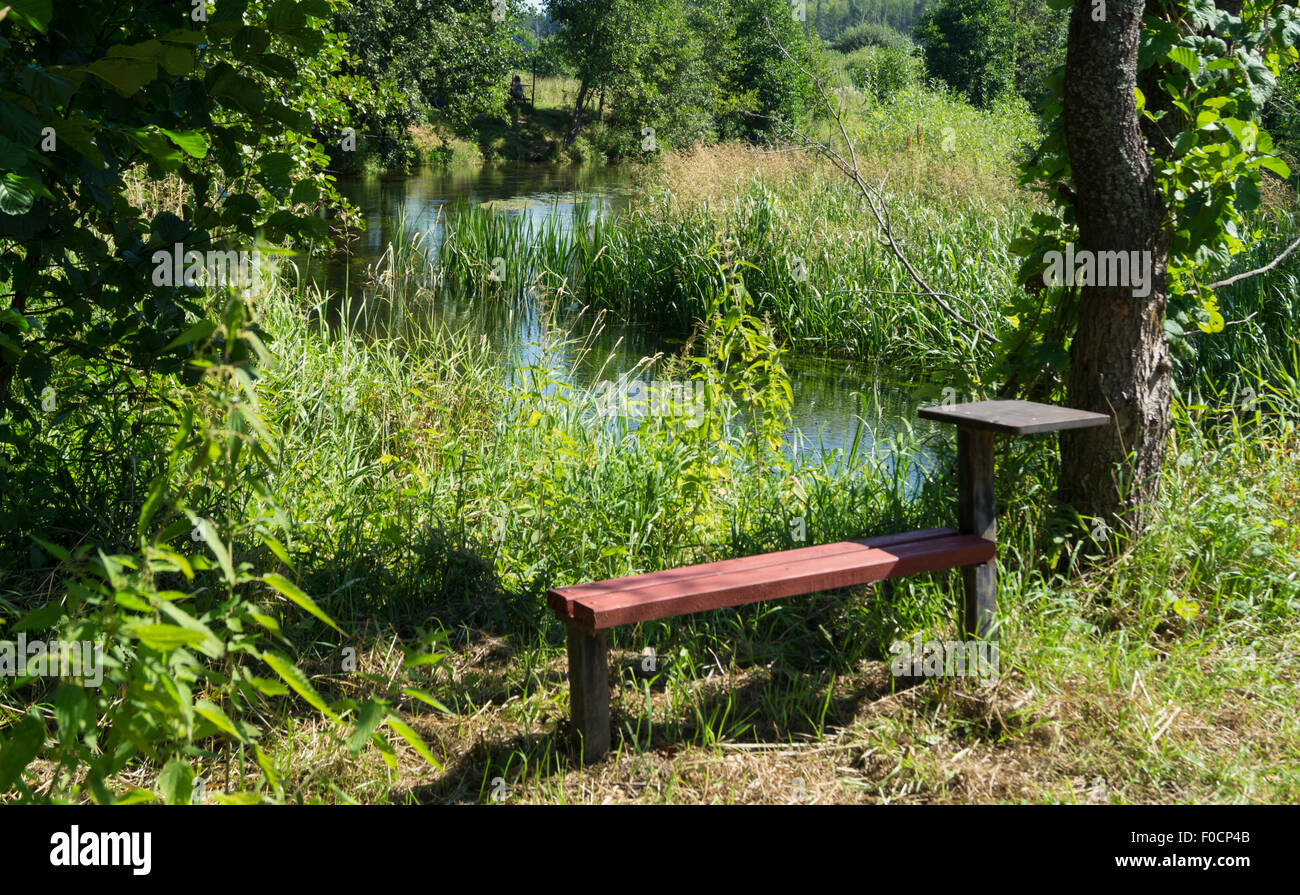 Landscape with small bench and table ashore small stream Stock Photo
