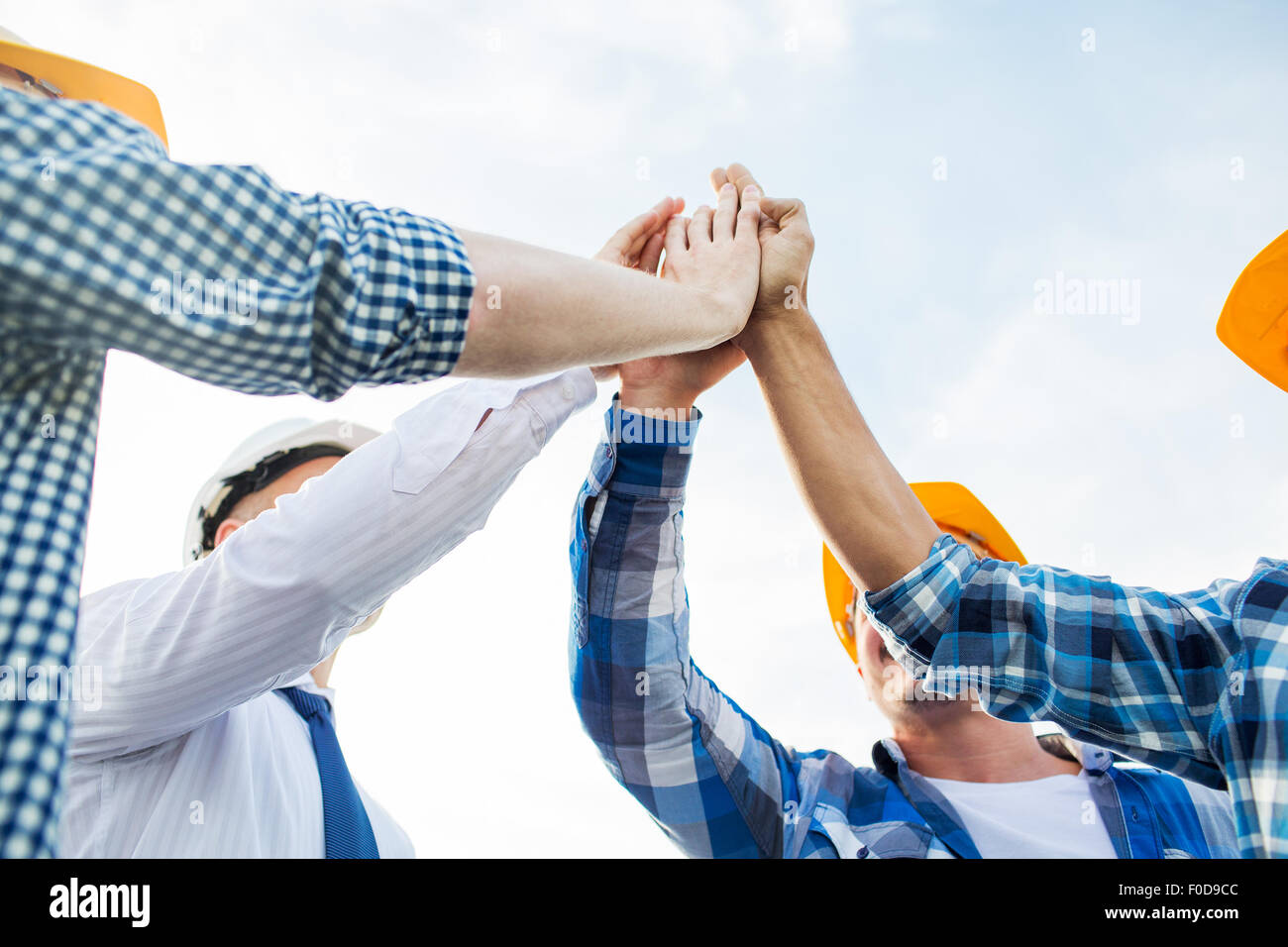 close up of builders in hardhats making high five Stock Photo