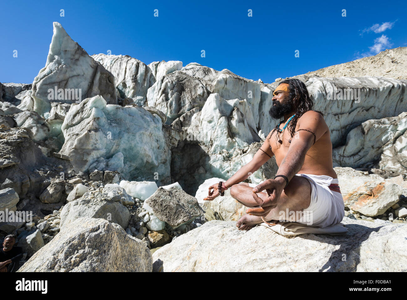 A Sadhu, holy man, is sitting in lotus pose, padmasana, on a rock at Gaumukh, the main source of the holy river Ganges, Gangotri Stock Photo