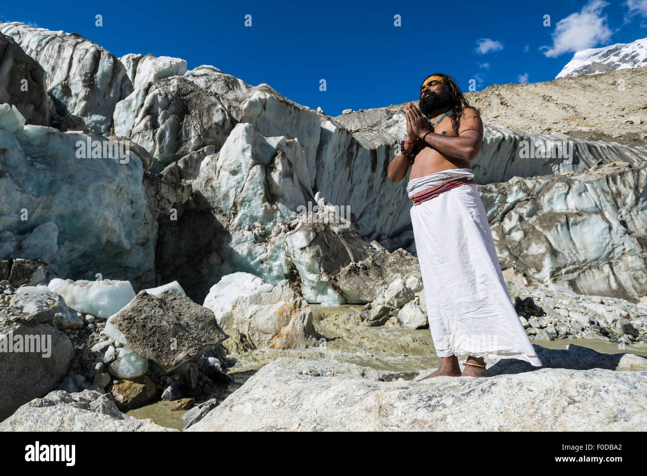 A Sadhu, holy man, is standing and praying on a rock at Gaumukh, the main source of the holy river Ganges, Gangotri, Uttarakhand Stock Photo