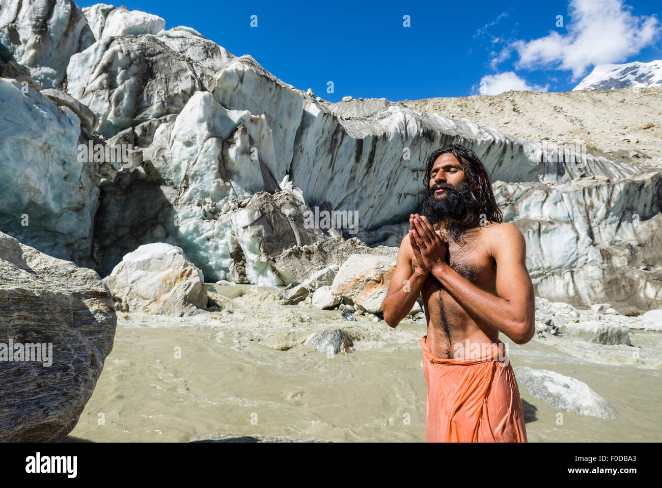 A Sadhu, holy man, is standing and praying on a rock at Gaumukh, the main source of the holy river Ganges, Gangotri, Uttarakhand Stock Photo